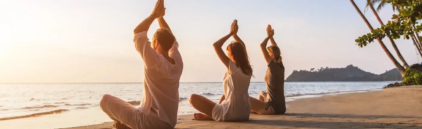 three people practice meditation on the beach